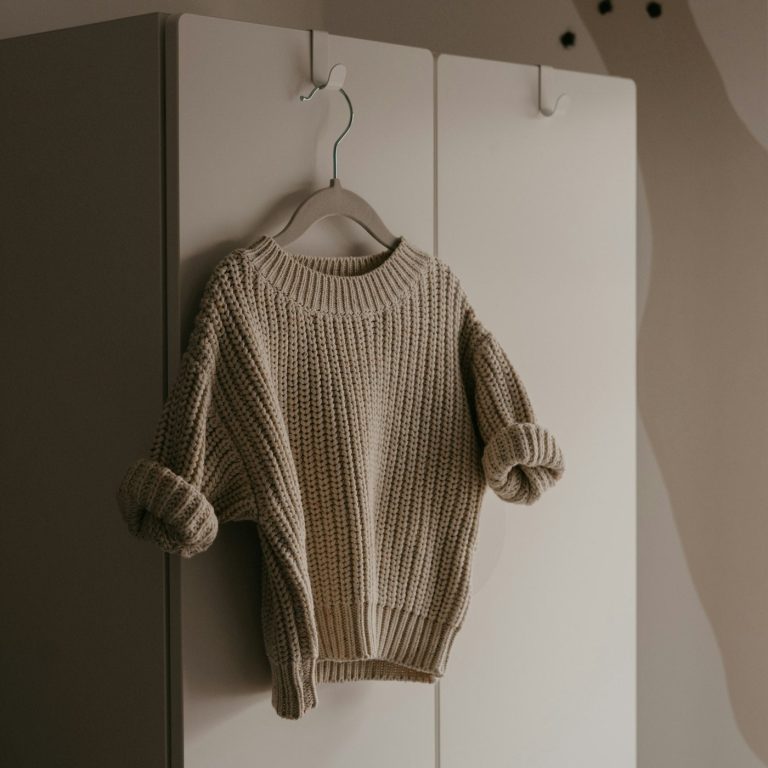 An oatmeal chunky knit child's jumper on a wooden hanger