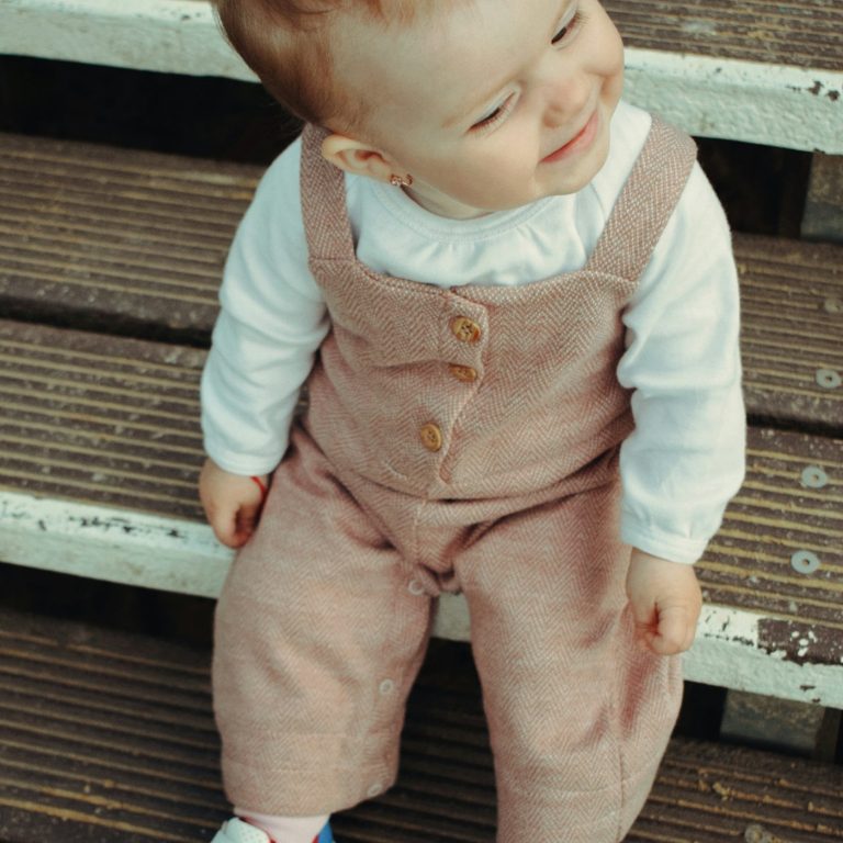A baby in soft pink corduroy dungarees with wooden buttons